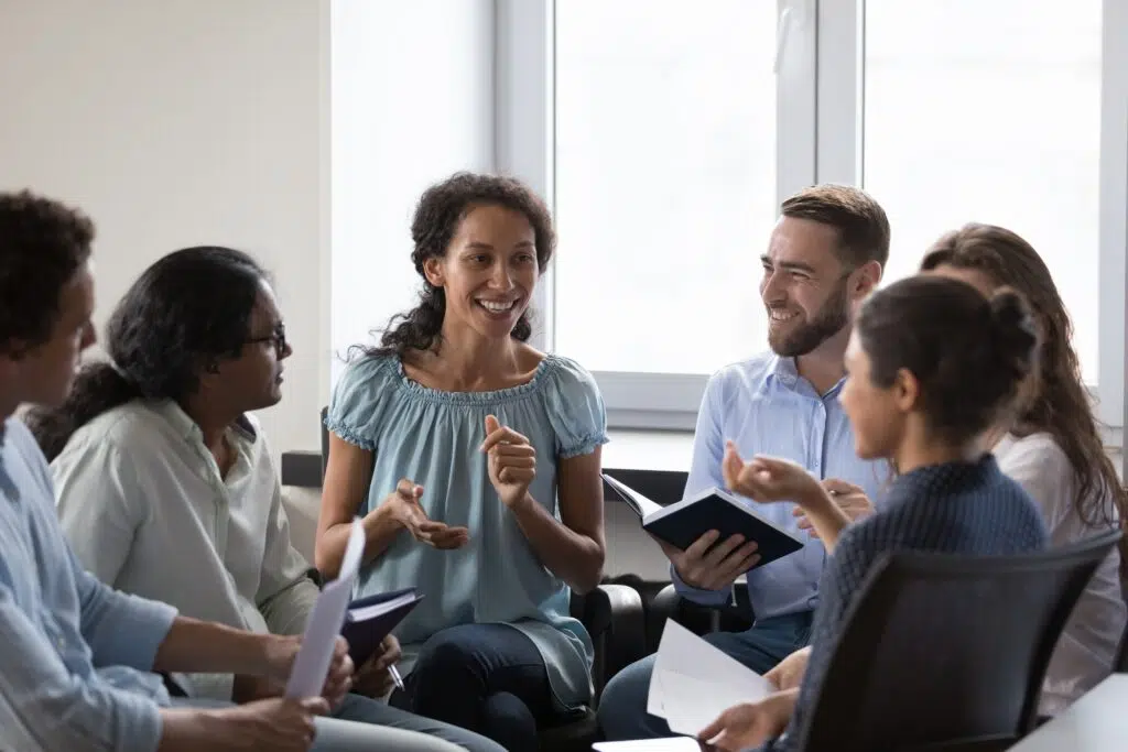 A diverse group of adults sitting in a circle, smiling and sharing during a support group meeting.