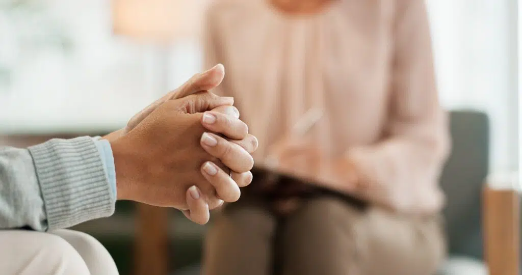 Close-up of a person sitting with hands clasped nervously while speaking with a therapist during a counseling session.