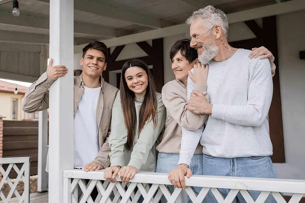 middle aged parents hugging and looking away near teenage daughter and adult son on porch
