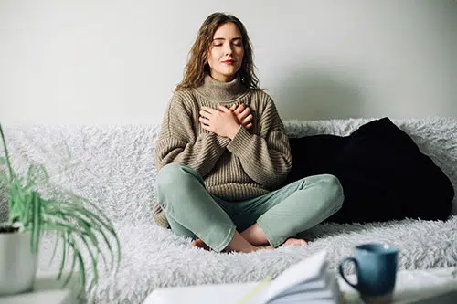 A young woman sits peacefully with her hands are crossed over her chest, reflecting calm and contemplation.