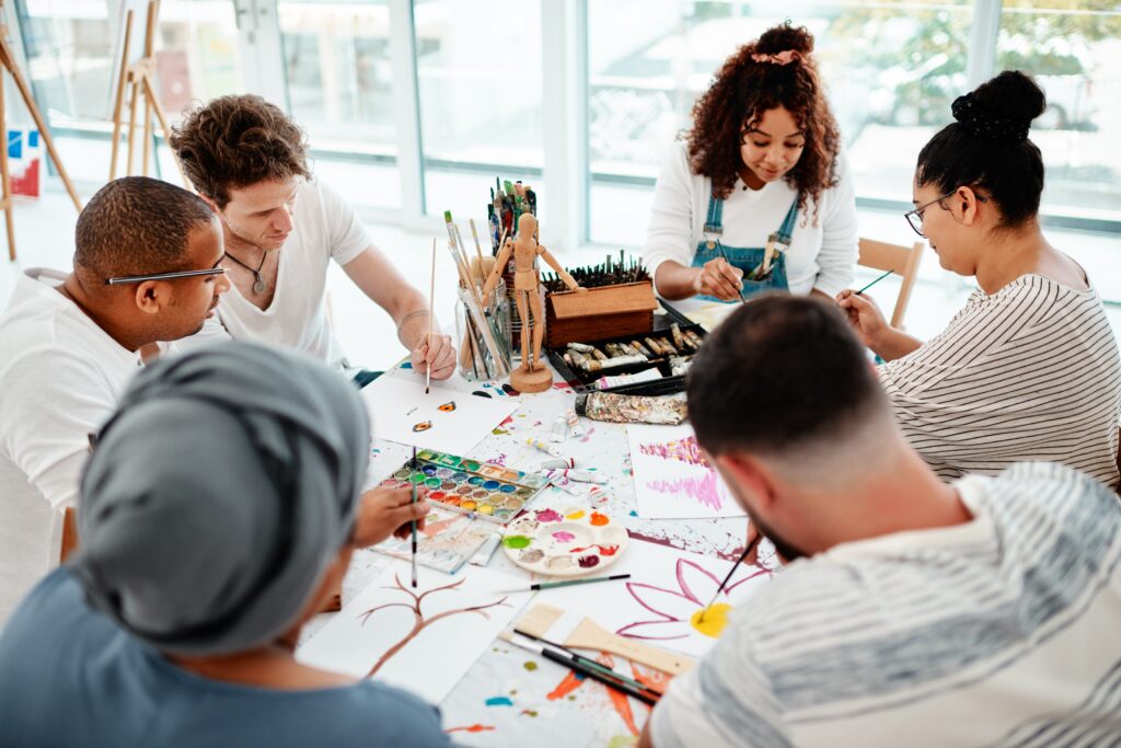 Group of adults painting together on canvases, smiling while creating colorful acrylic artwork during a class.