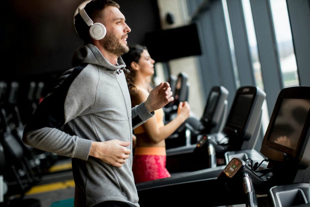 Young adults exercising on treadmills in a bright, modern fitness center with large windows