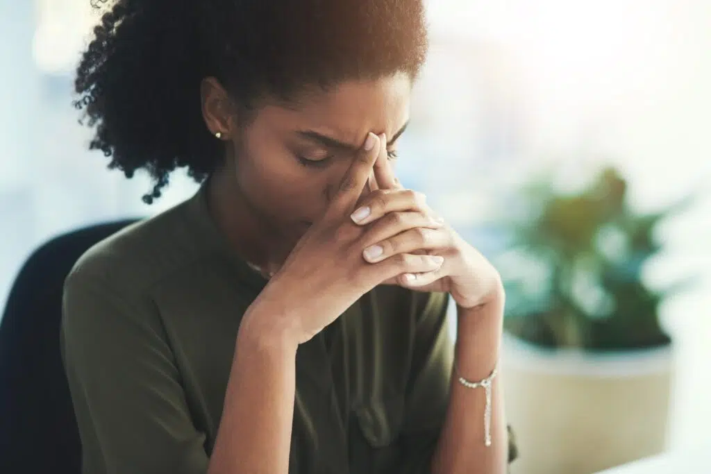 Businesswoman at desk holding her head with both hands, appearing stressed while working