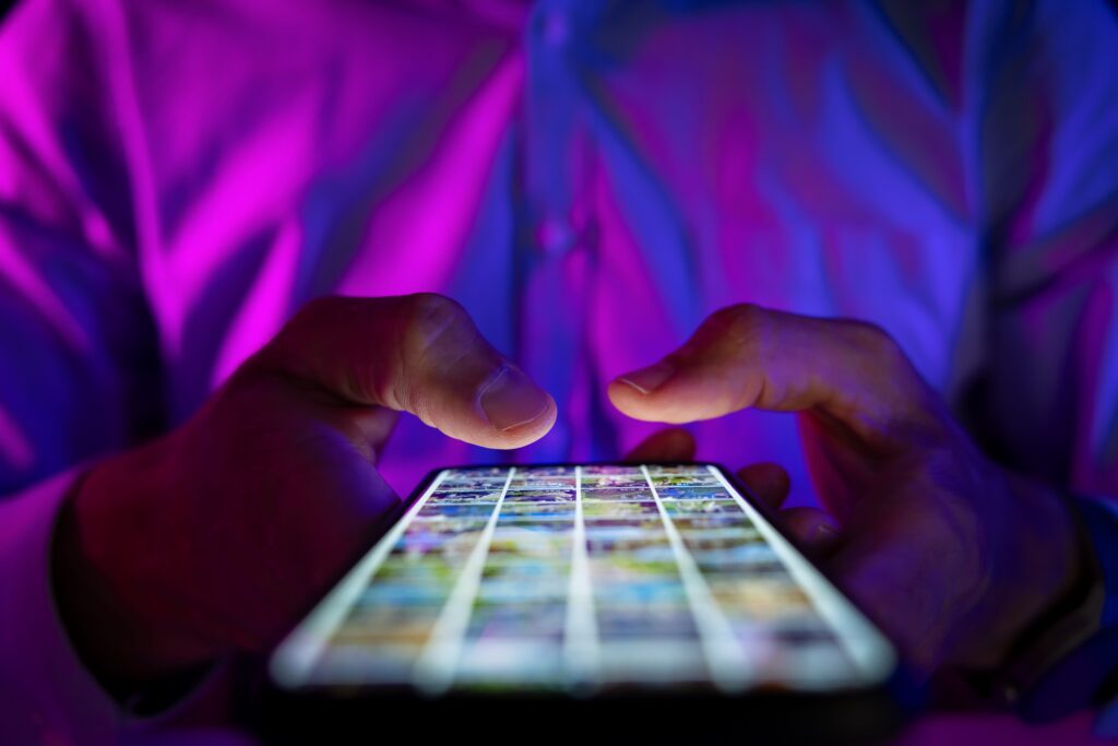 Man holding smartphone in dark room illuminated by blue and pink neon lights, browsing screen