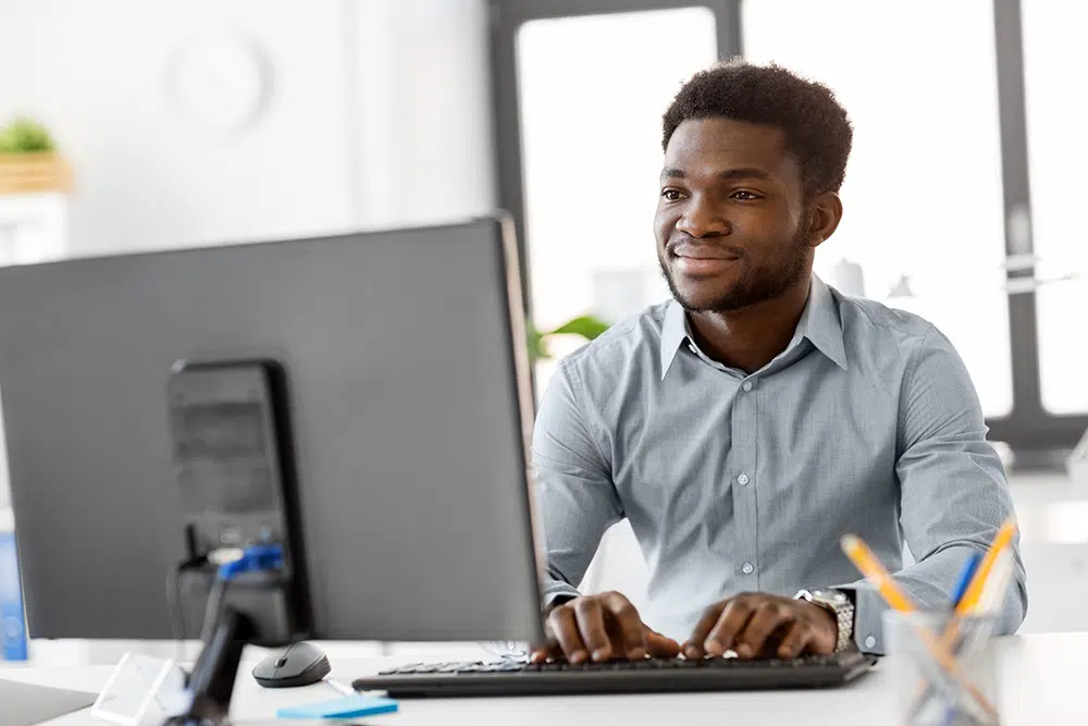 A young Black businessman works on his laptop in a modern office.