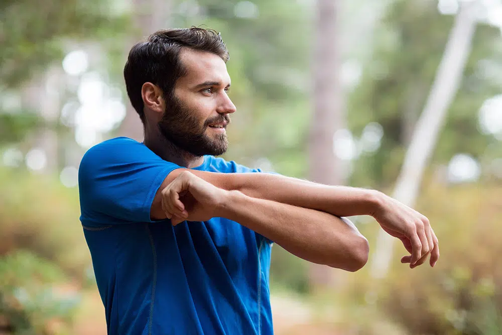 A male recovery patient stretches outside in a forest before exercising.
