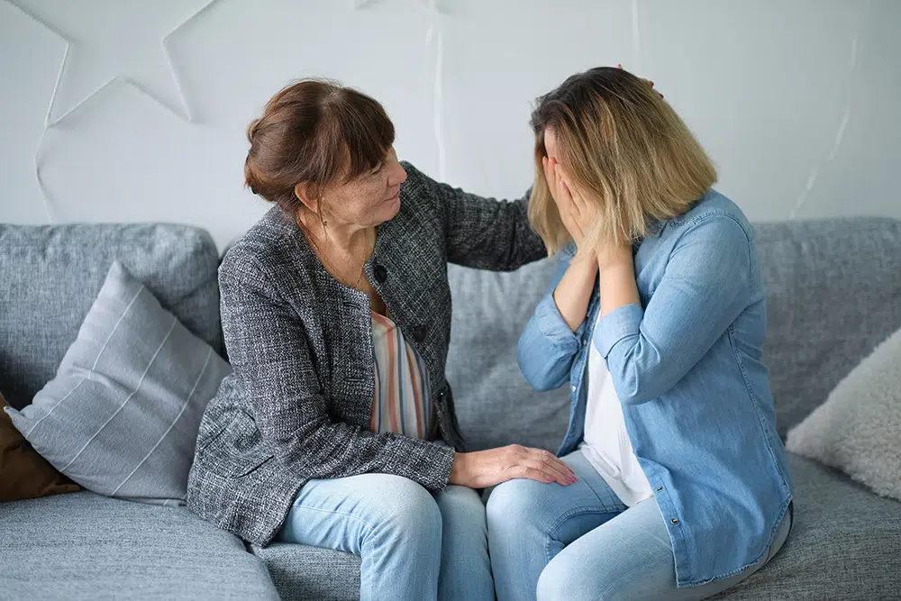 An elderly woman embraces and comforts her adult daughter who is crying because she needs help.