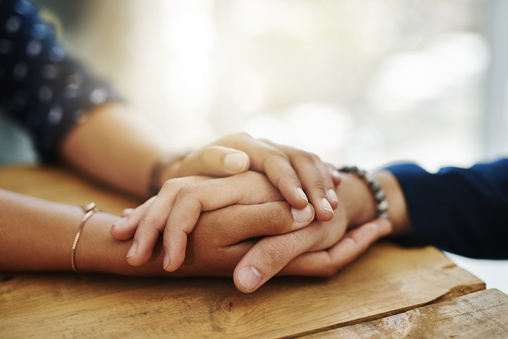 A closeup of a person’s hands holding another person’s hands as a gesture of comfort.